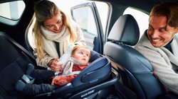 Moeder zet baby in een Maxi-Cosi in de auto, vader zit voorin de auto