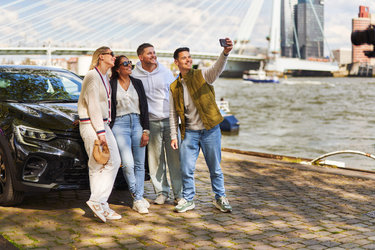 Jong volwassenen maken met de auto een selfie bij de Erasmusbrug.