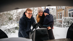 Gezin laadt bagage in de kofferbak van een huurauto op een winterse dag in een woonwijk