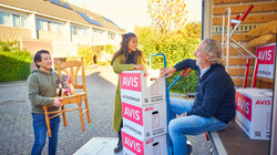 Three people stand on the tailgate of the moving van with moving boxes